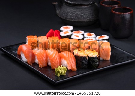 Close up of sashimi sushi set with chopsticks and soy on black background. Korea rolls and green tea cups and teapot, copy space. Japanese food.