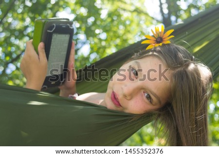 Young beautiful girl in hammock reading e-book. Pretty woman leisure lifestyle portrait at nature ountdoor. Female relax in forest. Adorable teen expressive face. Tourism in summer camp.