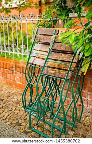 Folded garden chairs that lean against a fence on a rainy day.