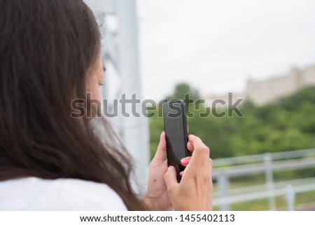 Young beautiful brunette tourist taking pictures on mobile phone, photographs the sights. Long-haired asian woman takes pictures, picture from the back, close view