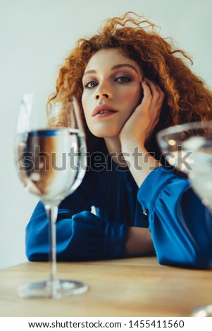 beautiful stylish redhead woman propping head and posing near glasses isolated on grey