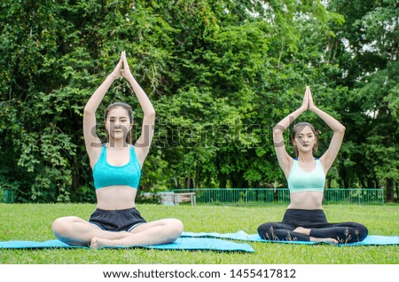 Two beautiful young woman sit meditation doing yoga in park. Relaxing and meditating while being surrounded by nature in summer park