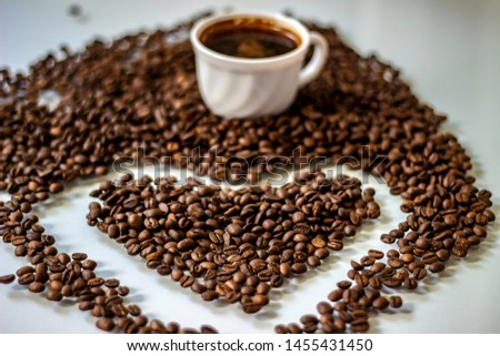 Coffee cup filled with beans and a heart of coffee beans. Coffee beans in the shape of a heart isolated on a white background. Heart shape made of perfect coffee beans, copy space. 