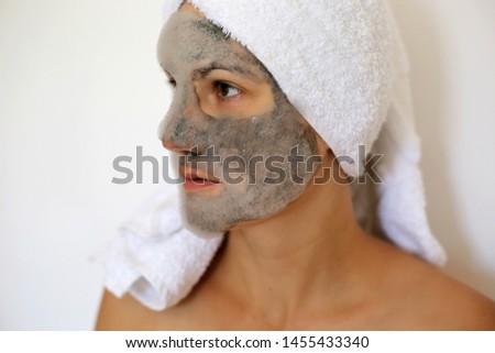 
Young woman with a black bubble charcoal oxygen mask on her face and towel on the head. Beauty spa acne treatment. Popular face mask.