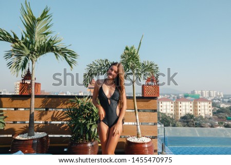 Portrait of a smiling caucasian woman in a swimsuit relaxing in a rooftop pool with green bushes and city views. Asia weekend