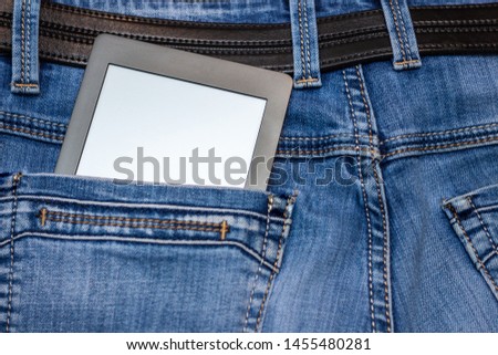 An e-reader hidden in a pocket of jeans pants. Close-up with selective focus. Copy space. Training and technology concept