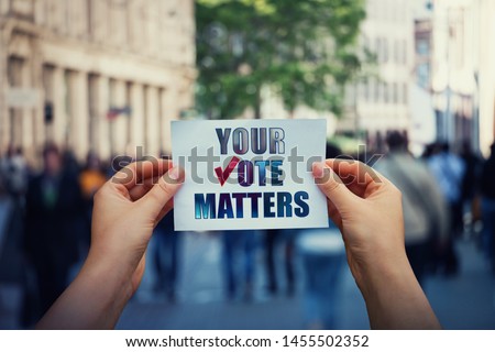 Hands hold a paper sheet with the message your vote matters over a crowded street background. People legal and democratic rights, every voice counts. Election campaign and electoral agitation concept.