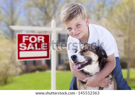 Happy Young Boy and His Dog in Front of For Sale Real Estate Sign and House.