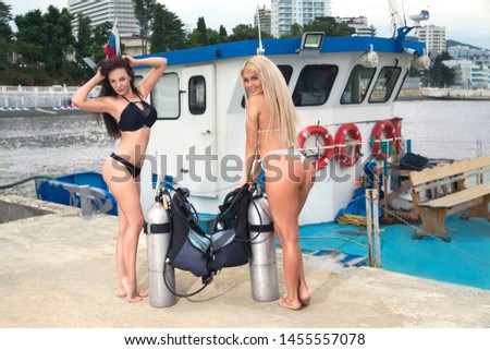 beautiful girls with diving equipment posing on the background of the ship and the sea