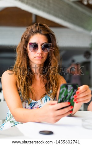 Portrait of the young woman in summer sitting at the restaurant on the vacation using mobile smart phone to send the message and check the pictures photos