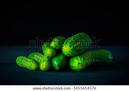 A bunch of fresh green cucumbers lying on a dark table. Side view. Plenty of room for text