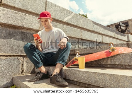 Skateboarder preparing for riding at the city's street in sunny day. Young man in sneakers and cap with a longboard on the asphalt. Concept of leisure activity, sport, extreme, hobby and motion.