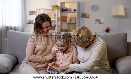 Happy female family members watching photo album pictures, having fun together