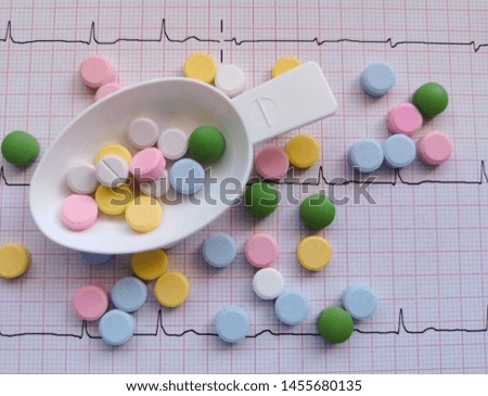 Photo of spoon, taking medicine and various color pills on the background. ECG type, atrial fibrillation.