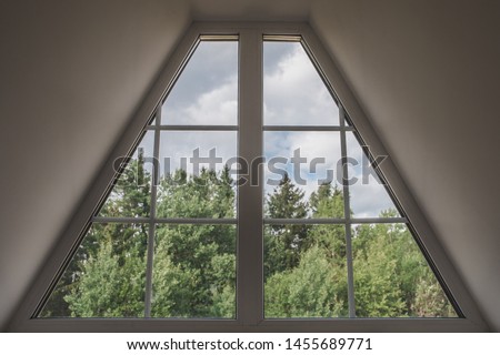 Inside view of the trapezoid-shaped attic window - idyllic landscape outside the window - forest and sky