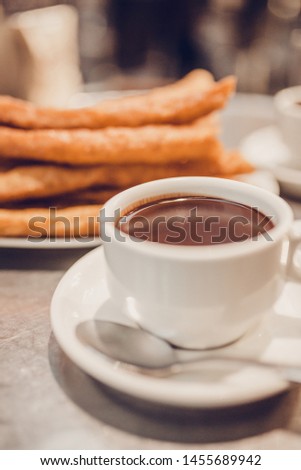 A cup of hot chocolate on the table next to a plate of churros - a very sweet dessert