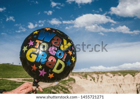 A closeup of a black balloon with a writing "Way to go Grad" held by a person in the desert