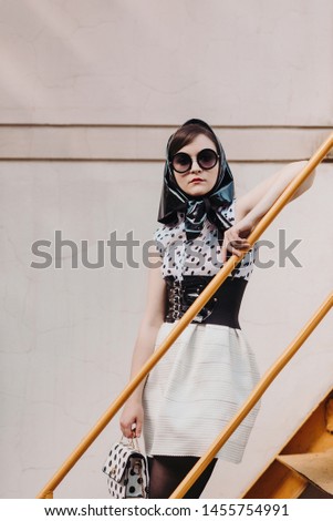 The concept of fashionable winter and black and white colors. Stylish woman in a black and white polka dot dress is standing on a urban background with different emotions.