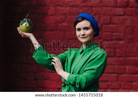 The concept of fashionable summer, blue and green colors. Stylish young woman in blue beret and skirt with a green shirt is standing against a red brick wall close up