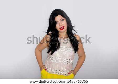 Portrait of a beautiful young brunette isolated on white background. Woman posing in the studio. White shiny blouse and yellow pants.