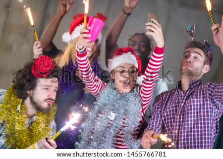 multiethnic group of young happy casual business people taking selfie picture while dancing with sparklers and having fun during new year party in front of concrete wall at new startup office