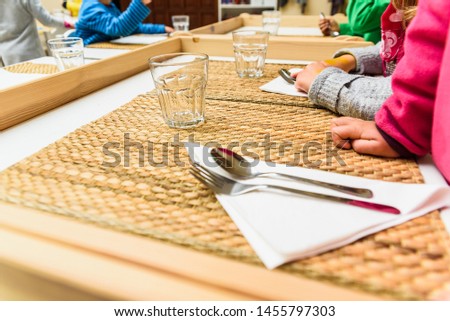 Children sitting at the table in a school cafeteria while the teachers serve them food.
