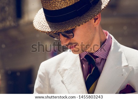 Young dandy wearing a tie, a red pocket handkerchief and a straw boater hat, taking a stroll in the streets of an Italian town Royalty-Free Stock Photo #1455803243