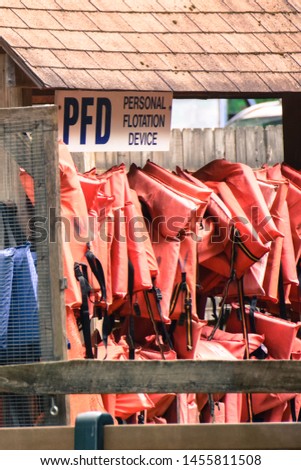 signage that reads PFD Personal Floatation Device and several  orange life jackets hung in two rows in a wooden hanging hut