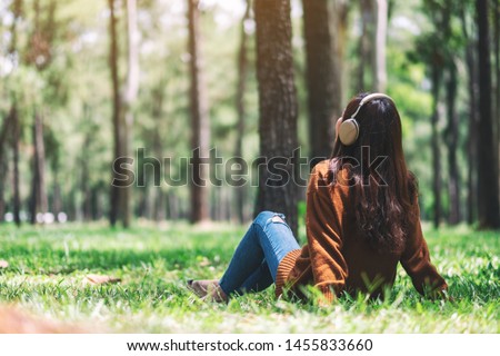 A beautiful asian woman enjoy listening to music with headphone with feeling happy and relaxed in the park Royalty-Free Stock Photo #1455833660