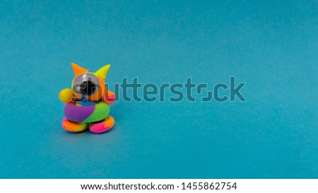 handmade clay monster of multiple colors in a minimal blue background