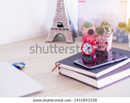 Red alarm clock with phone on books blurred background,selective focus.