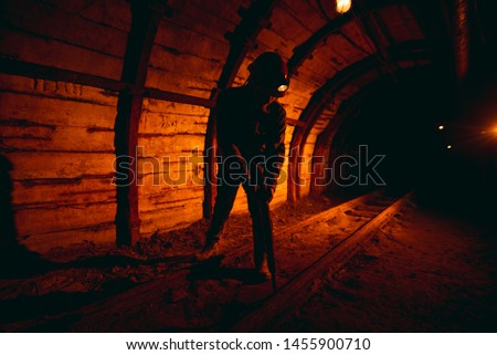 A man in work overalls and a helmet with a jackhammer on his shoulder is standing on the rails. Silhouette in red. Mine worker. Miner Royalty-Free Stock Photo #1455900710