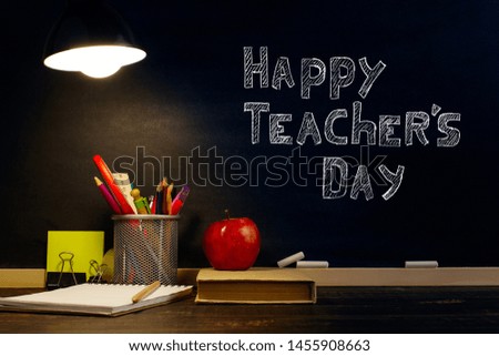 The teacher's desk or a worker, on which the writing materials lie, a book and an apple, in the evening under the lamp. Blank for text or background for a school theme. Copy space.