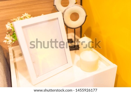 Room decoration, white picture frame, white candle, flower vase, and yellow wall