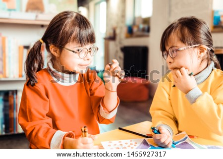 Sister catching inspiration. Cute children with down syndrome talking to each other and discussing idea of a new picture