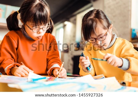 Creating with sister. Little concentrated kids with down syndrome working on a new picture while having developing classes