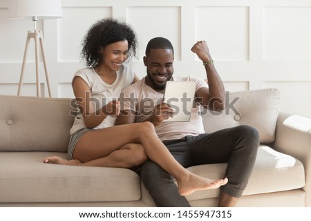 Excited happy african family couple looking at digital tablet feel winners overjoyed by lottery winning bet bid, celebrate good internet news, euphoric with great online victory prize new sale offer Royalty-Free Stock Photo #1455947315