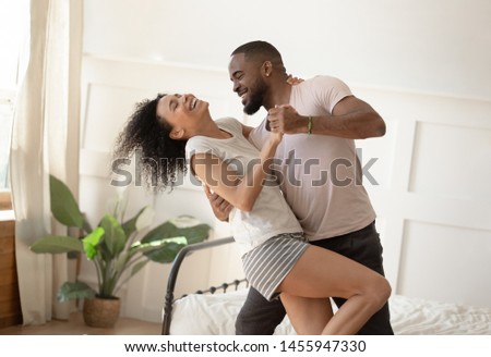 Happy romantic young black couple dancing bonding laughing in bedroom, carefree active millennial african american man and woman enjoying moments of love and affection at home in the morning