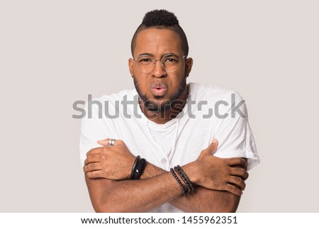 Unhappy African American man in glasses looking at camera, stressed young male feeling cold, freezing, shivering, hugging warming himself, low temperature, isolated on studio background Royalty-Free Stock Photo #1455962351