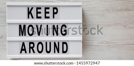 A lightbox with 'Keep moving around' words over white wooden background, top view. From above, flat lay, overhead. Copy space.
