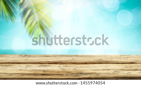 Wooden table top background with beautiful calm ocean outside. Some palm leaves above the table top. Empty space for an advertising product.