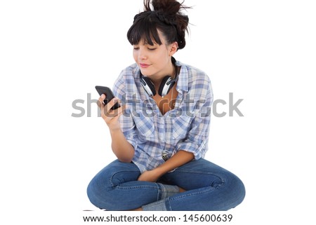 Smiling young woman sitting on the floor with headphones holding her mobile phone on white background