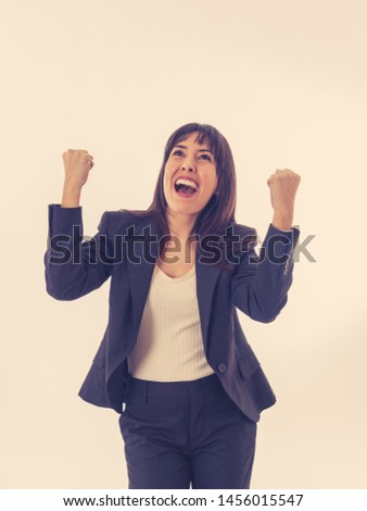 Close up of a young business woman standing isolated celebrating on neutral background. Smiling with arms up feeling happy and successful. In people business education, success concept.