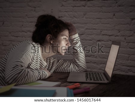 Overworked and tired female student working late at night on her laptop trying not to fall asleep feeling fatigued, worried and sad. Moody dark light. Online learning and stress work concept.