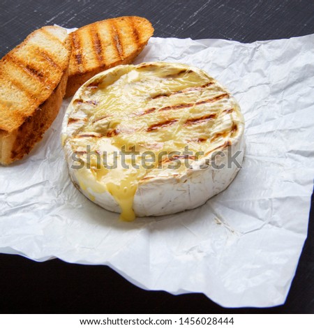 Grilled camembert cheese on a black surface, side view. Close-up.