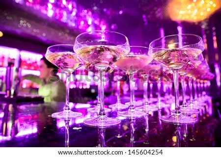 Glasses of champagne on bar counter with barman professional, which making cocktail drinks in background, soft focus Royalty-Free Stock Photo #145604254