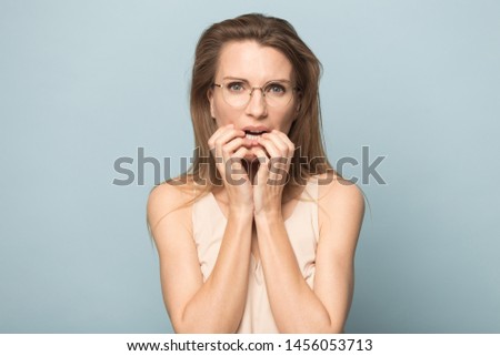 Nervous scared woman in glasses biting nails, feeling fear, stressed attractive female student, businesswoman thinking about problem, anxious, looking at camera, isolated on studio background