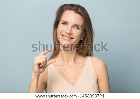 Smiling happy woman showing little size gesture with fingers, small prices, shopping sales price decrease, something tiny, attractive female looking at camera, isolated on grey studio background