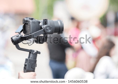 Video shooting with a camera with a tripod with a black stabilizer. The background is blurred. 