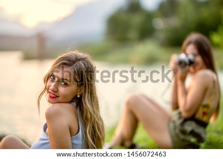 two young beautiful happy stylish hipster girls,  denim outfit, smiling, happy, cool accessories,  having fun, sitting, park, sneakers, portraits, camera, take photo